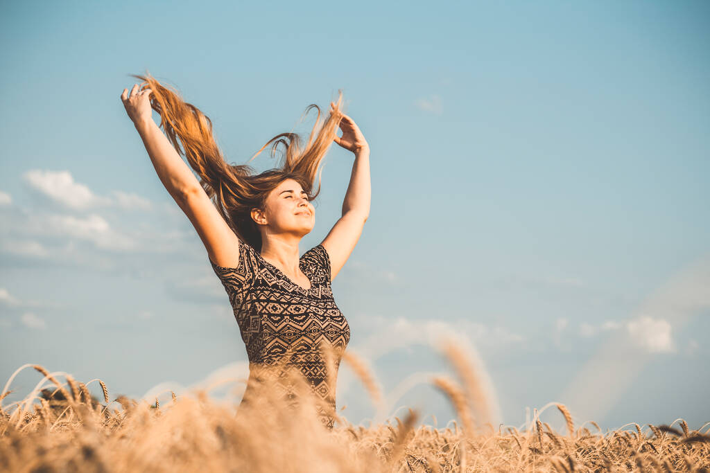 szczęśliwa piękna młoda kobieta ciesząca się przyrodą, podnosząc ręce na tle zachmurzonego nieba na polu pszenicy, dziewczyna oddycha głęboko, wolność i relaks koncepcja - Zdjęcie, obraz