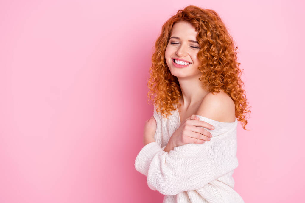 Φωτογραφία πορτρέτο του κόκκινα μαλλιά σγουρά γυναίκα χαμογελώντας αγκαλιά με τον εαυτό ονειρικό απομονωμένο σε παστέλ ροζ χρώμα φόντο με κενό χώρο - Φωτογραφία, εικόνα