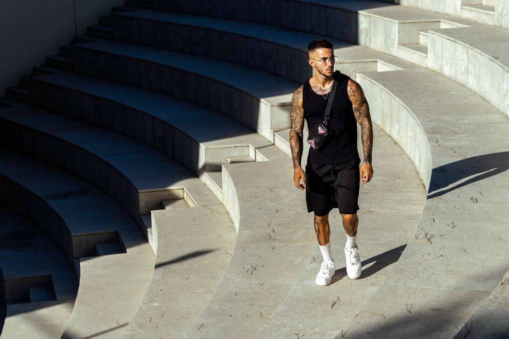 Un maschio sportivo caucasico con tatuaggi in piedi nella scala di pietra architettura - Foto, immagini