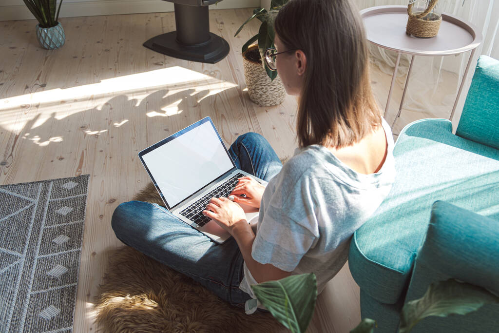 Junge Frau nutzt Laptop-Bildschirm zur Arbeit, sitzt zu Hause auf dem Boden, Flexible Arbeitszeiten und Fernarbeit - Foto, Bild