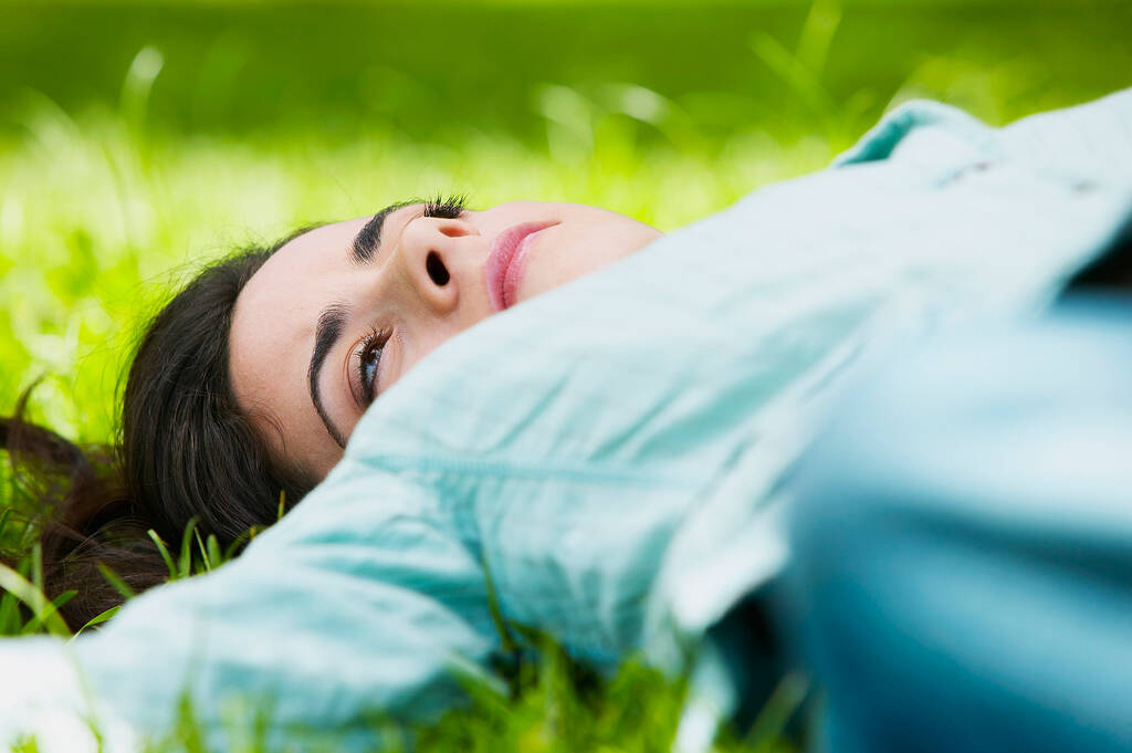 Nuori nainen makaa vihreällä ruoholla puistossa - Valokuva, kuva