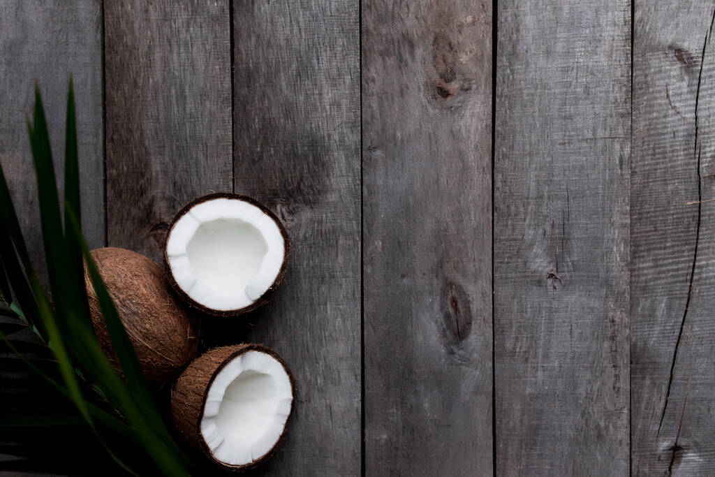 Złamane kokosy na szarym drewnianym tle z liściem palmy. Biała miazga kokosowa. Wysokiej jakości zdjęcie - Zdjęcie, obraz