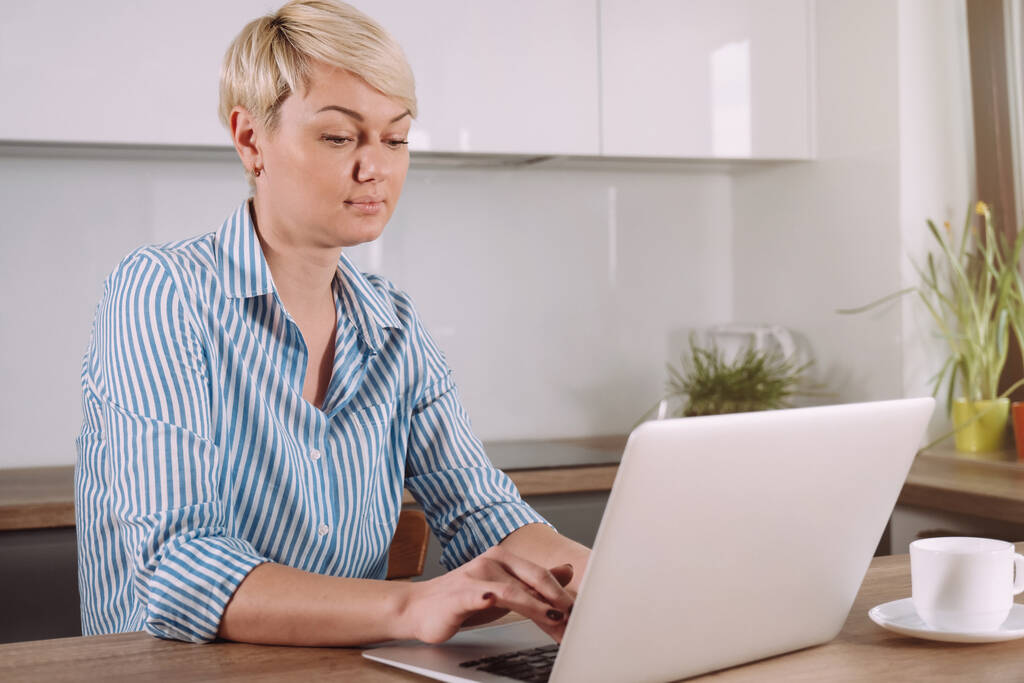 Mujer de negocios que trabaja a través de una computadora portátil sentada en la cocina en casa, freelancer concepto de proceso de trabajo usando computadora portátil - Foto, Imagen