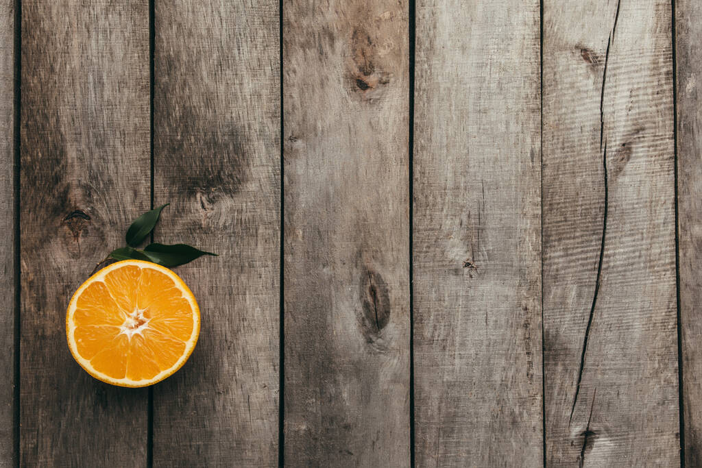 Pokrojone połówki pomarańczowych owoców na szarym drewnianym tle. Miąższ i zielone liście. Wysokiej jakości zdjęcie - Zdjęcie, obraz