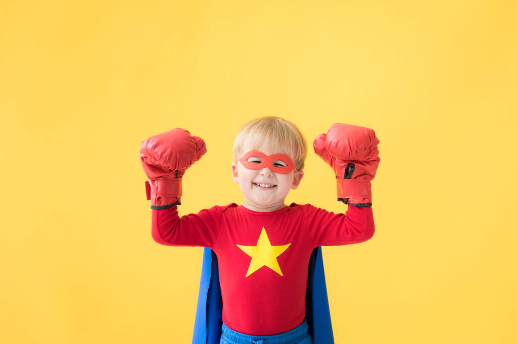 Retrato del niño superhéroe. Super héroe niño contra el fondo de papel amarillo. Niño feliz vistiendo máscara roja y capa de superhéroe. Los niños sueñan y concepto imaginación - Foto, Imagen