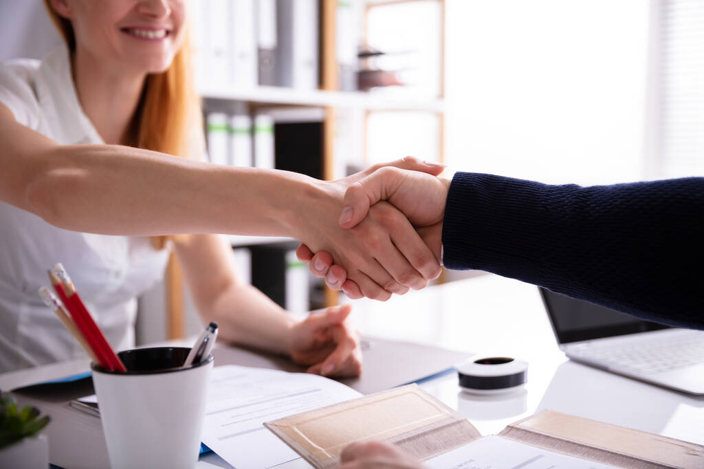 Empresária sorridente apertando a mão com seu colega sobre mesa no local de trabalho
 - Foto, Imagem