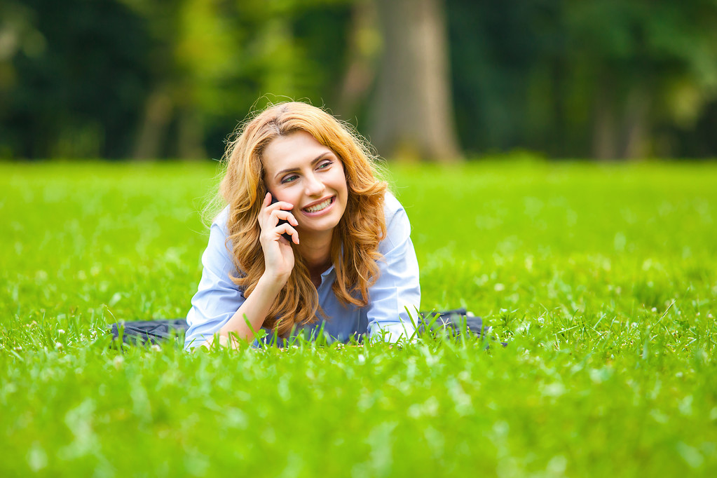 blonde vrouw spreken op cellphone in groene gras - Foto, afbeelding