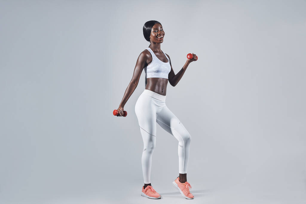 Hermosa joven africana en ropa deportiva haciendo ejercicio con pesas - Foto, imagen
