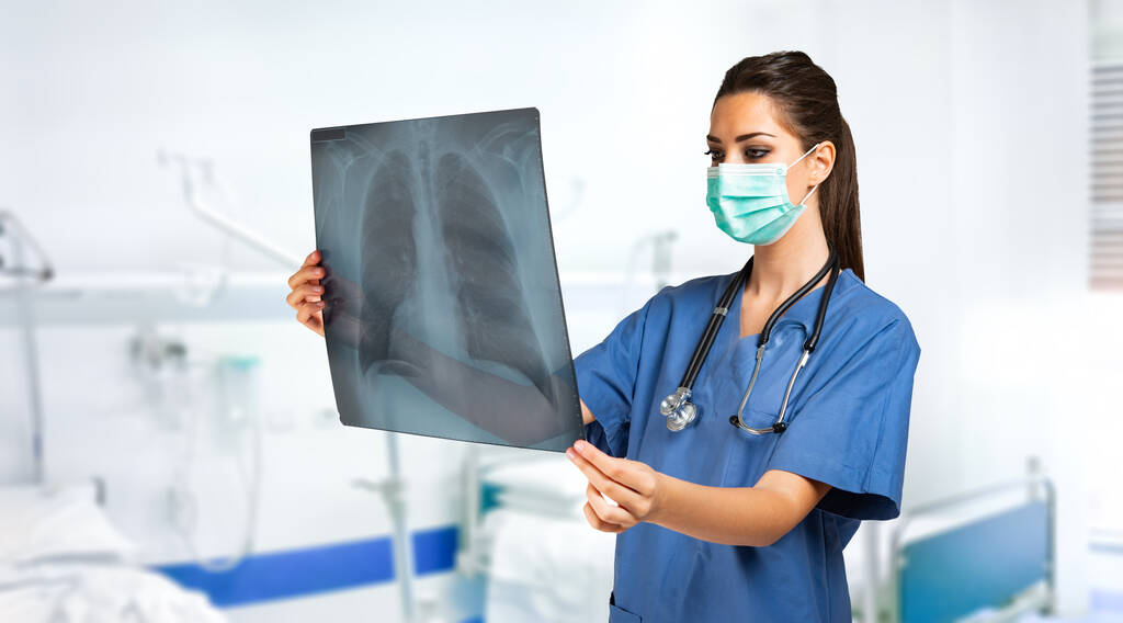 Mladá maskovaná zdravotní sestra se dívá na radiografii, kovid a koronavirus koncept - Fotografie, Obrázek