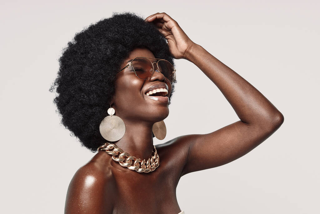 mooie jonge Afrikaanse vrouw in gouden sieraden houden ogen dicht en glimlachen - Foto, afbeelding
