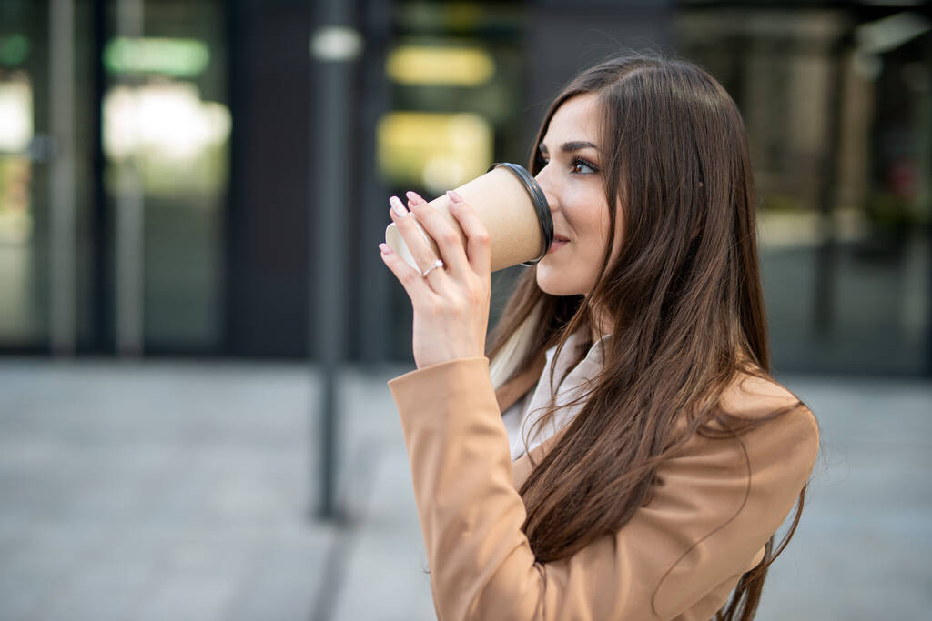Молодая деловая женщина пьет кофе во время прогулки по городу - Фото, изображение