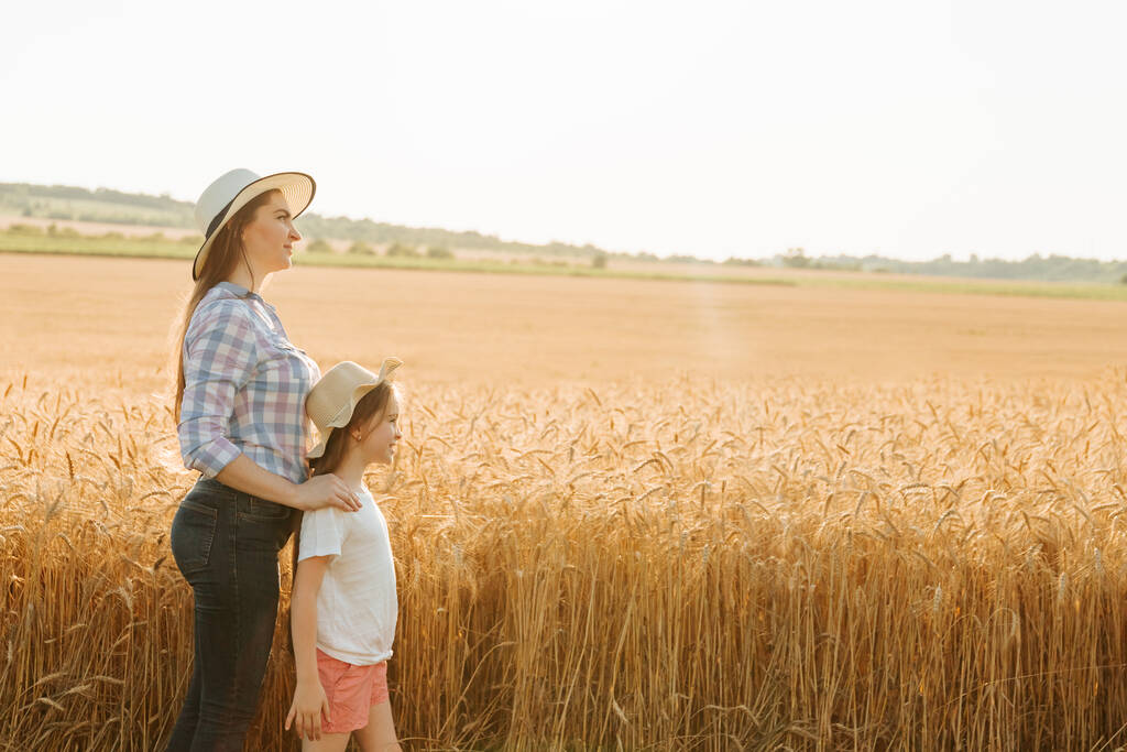 widok z boku, portret rodziny rolników matka z córką w kapeluszach na złotym polu pszenicy - Zdjęcie, obraz
