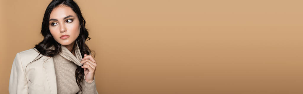 femme brune ajustant col roulé et regardant loin isolé sur beige, bannière - Photo, image