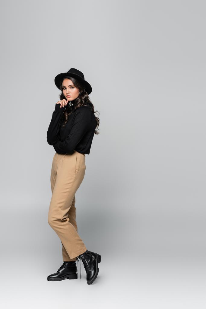 comprimento total de modelo muito jovem em chapéu fedora preto e roupa elegante posando em cinza - Foto, Imagem