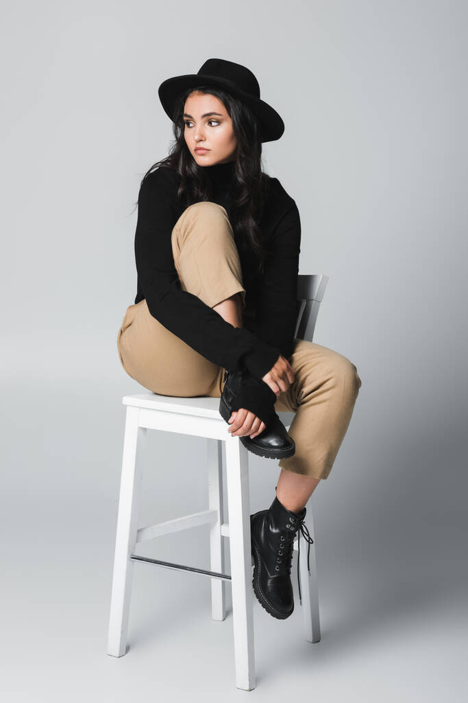 teljes hossza fiatal divatos nő fedora kalap ül széken szürke  - Fotó, kép