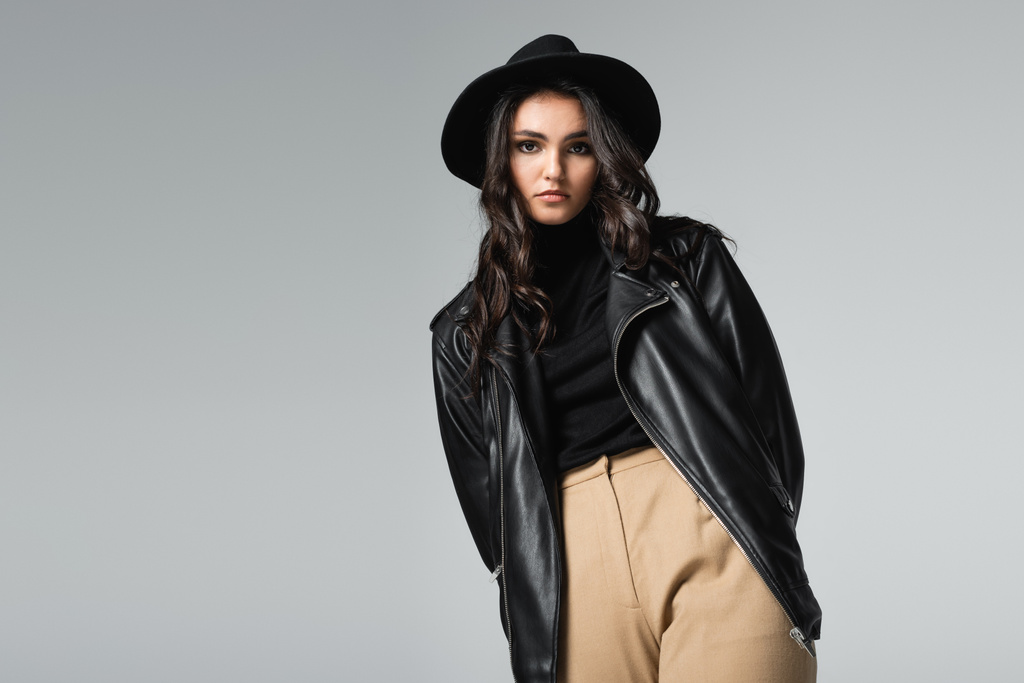 giovane donna in cappello fedora e giacca di pelle alla moda posa isolata sul grigio - Foto, immagini