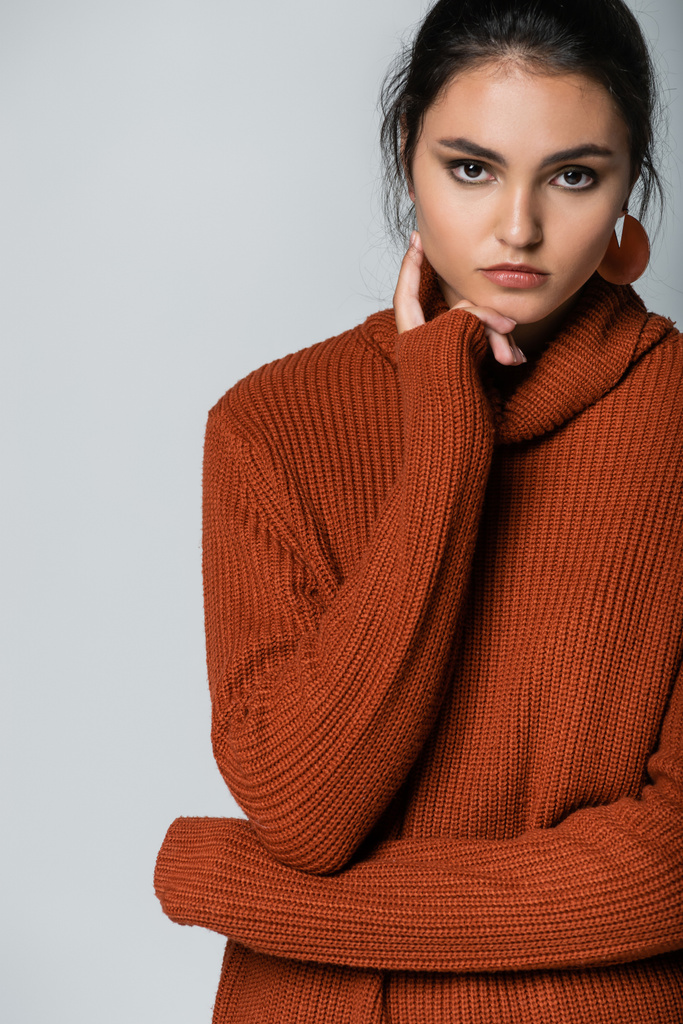 young model in earrings and knitted sweater looking at camera isolated on grey - Photo, Image