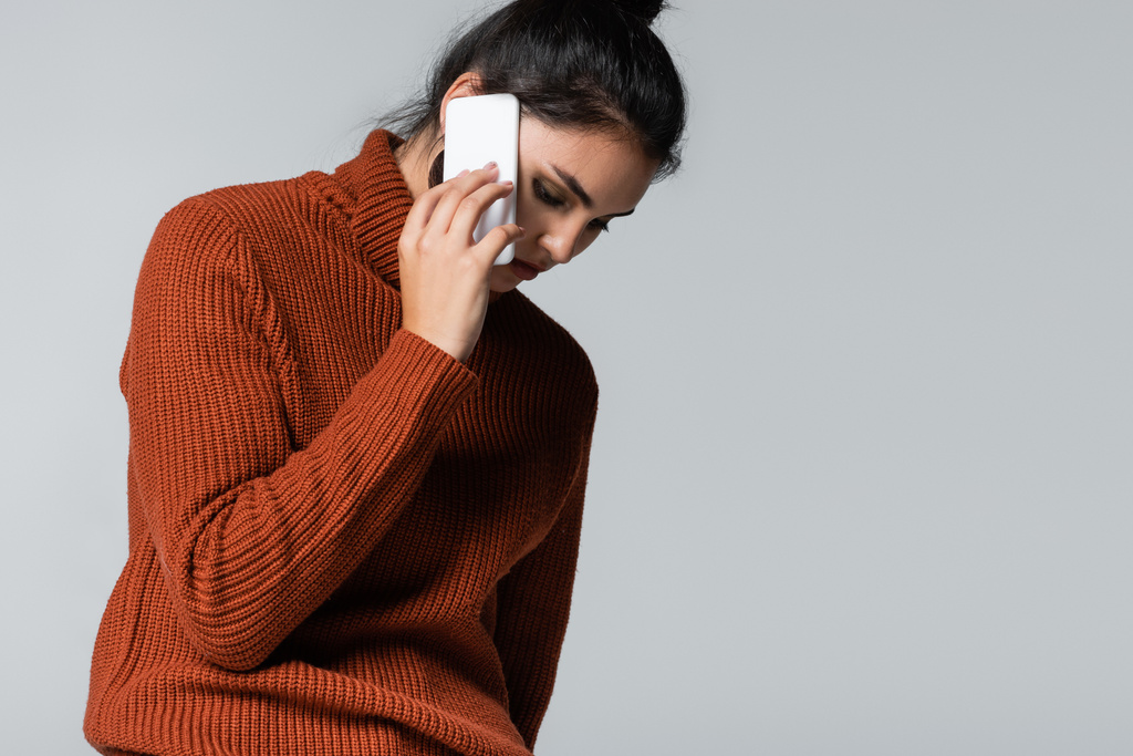 νεαρή γυναίκα σε πλεκτό πουλόβερ μιλώντας στο κινητό τηλέφωνο απομονώνονται σε γκρι - Φωτογραφία, εικόνα