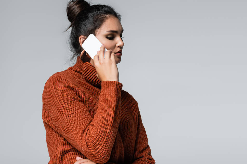 νεαρή γυναίκα με ζεστό πουλόβερ μιλώντας σε smartphone απομονωμένο σε γκρι - Φωτογραφία, εικόνα
