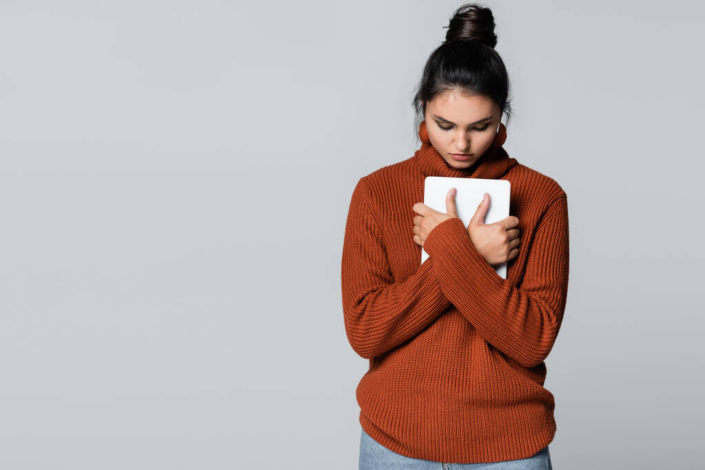 暖かいセーターを着た若い女性がグレーで隔離されたデジタルタブレットを持ち  - 写真・画像