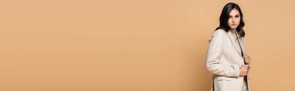 brunetka mladá modelka v módním obleku seřizování sako izolované na béžové, banner - Fotografie, Obrázek