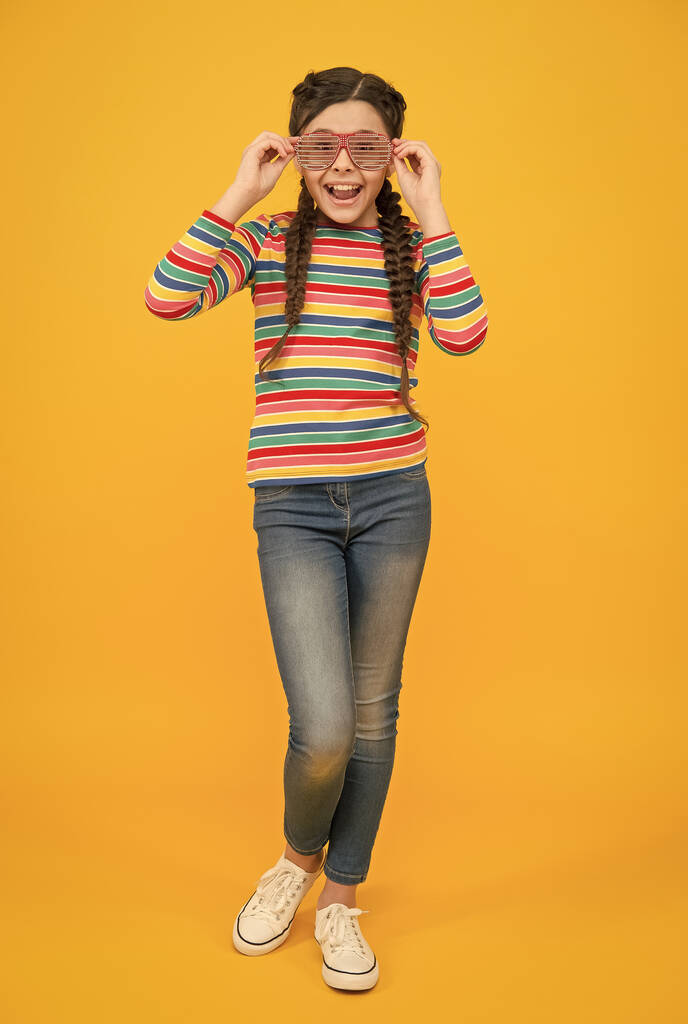 gelukkig tiener meisje met gevlochten haar dragen casual stijl regenboog kleur en glamour party bril op gele achtergrond, optimist - Foto, afbeelding