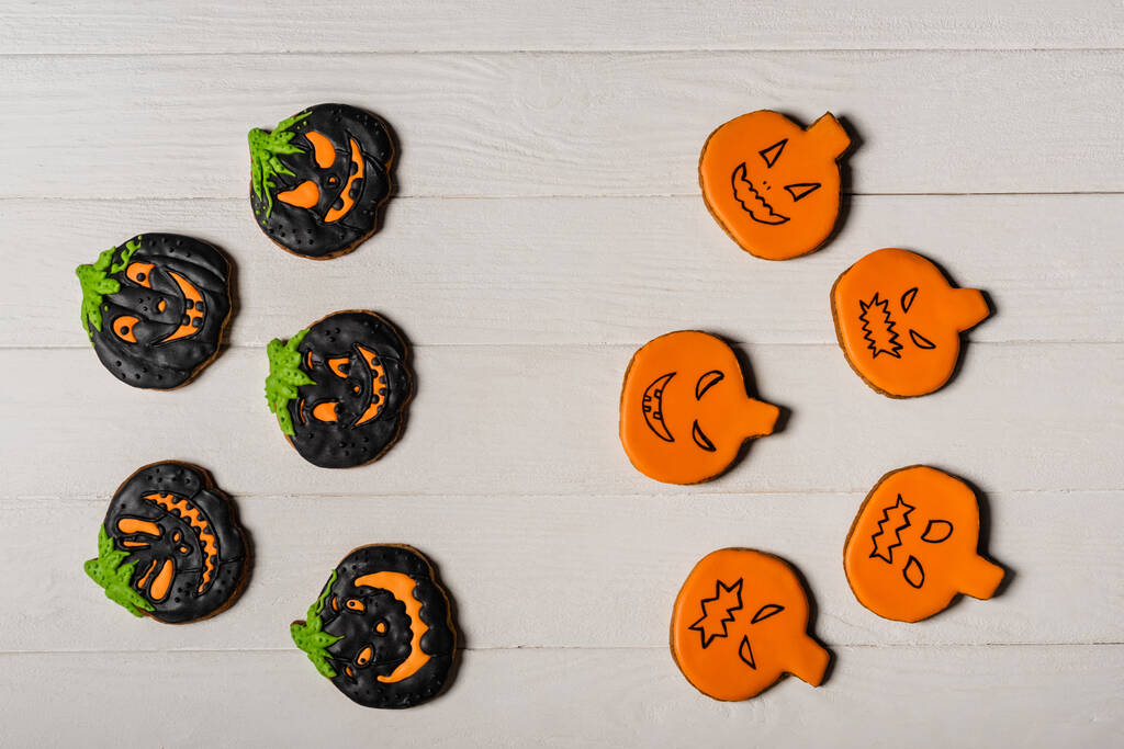 bovenaanzicht van zelfgemaakte en spookachtige pompoen vorm halloween koekjes op wit oppervlak - Foto, afbeelding