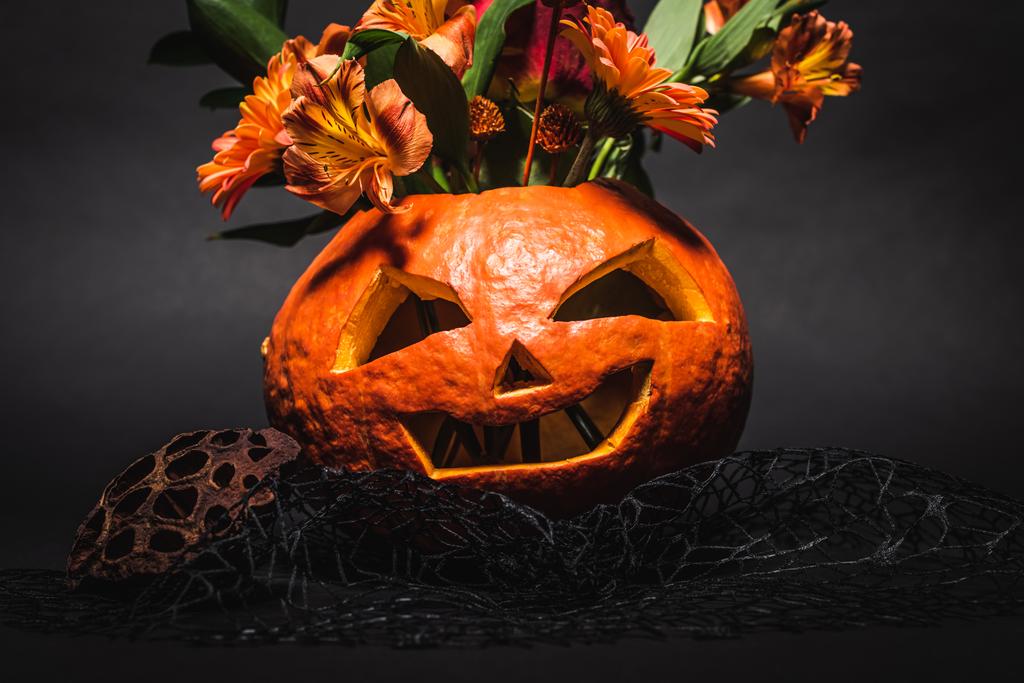flowers in spooky and carved orange pumpkin on black background  - Photo, Image