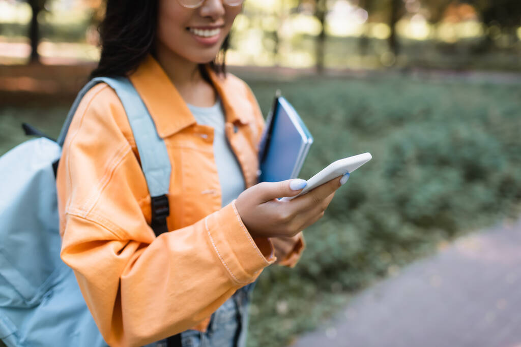 vista parziale della donna sfocata in giacca arancione utilizzando il telefono cellulare all'aperto - Foto, immagini