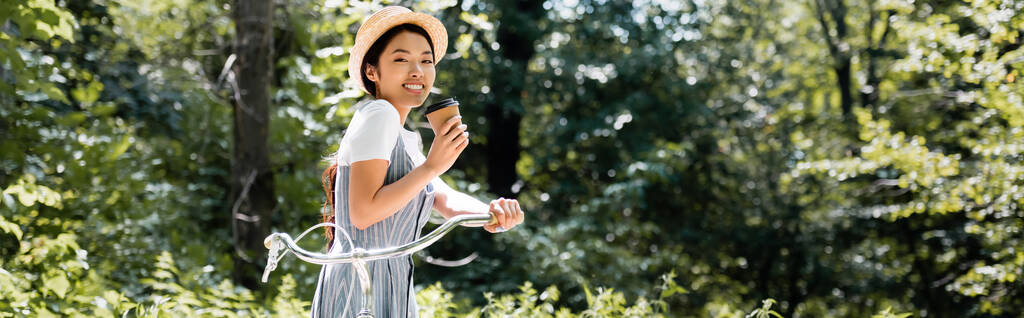 mladá asijská žena s bicyklem a odnést drink s úsměvem na kameru v parku, banner - Fotografie, Obrázek