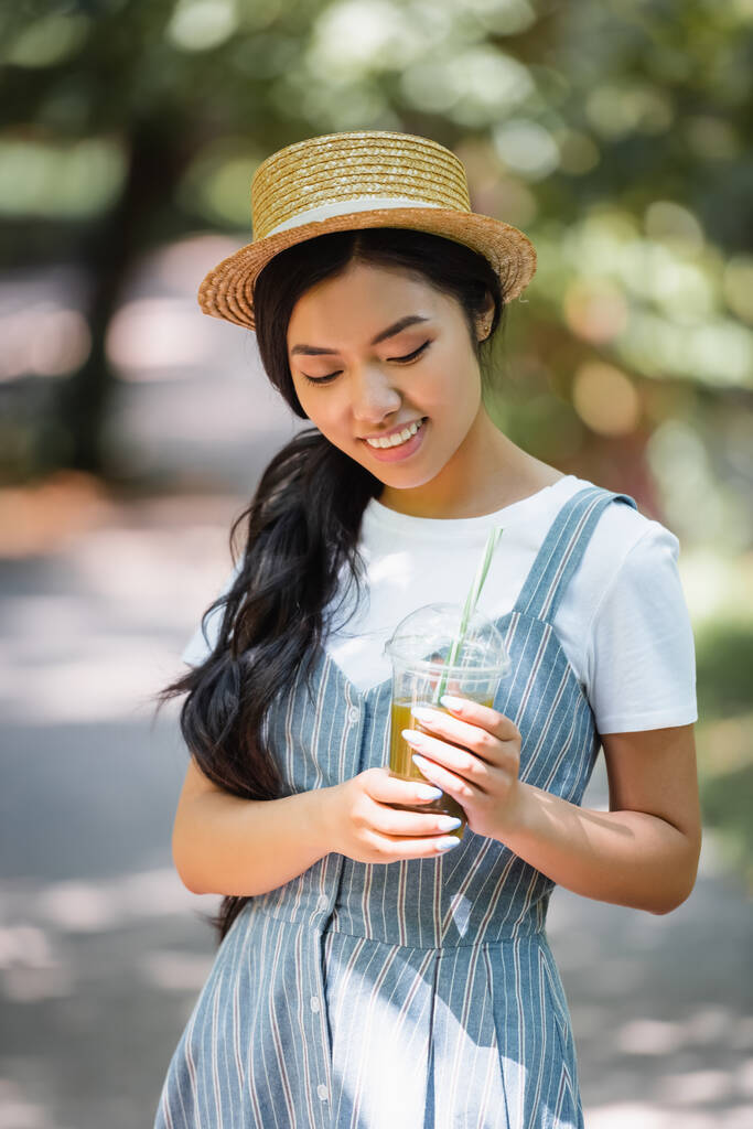 довольная азиатская женщина с пластиковой чашкой свежего сока, стоя на открытом воздухе - Фото, изображение