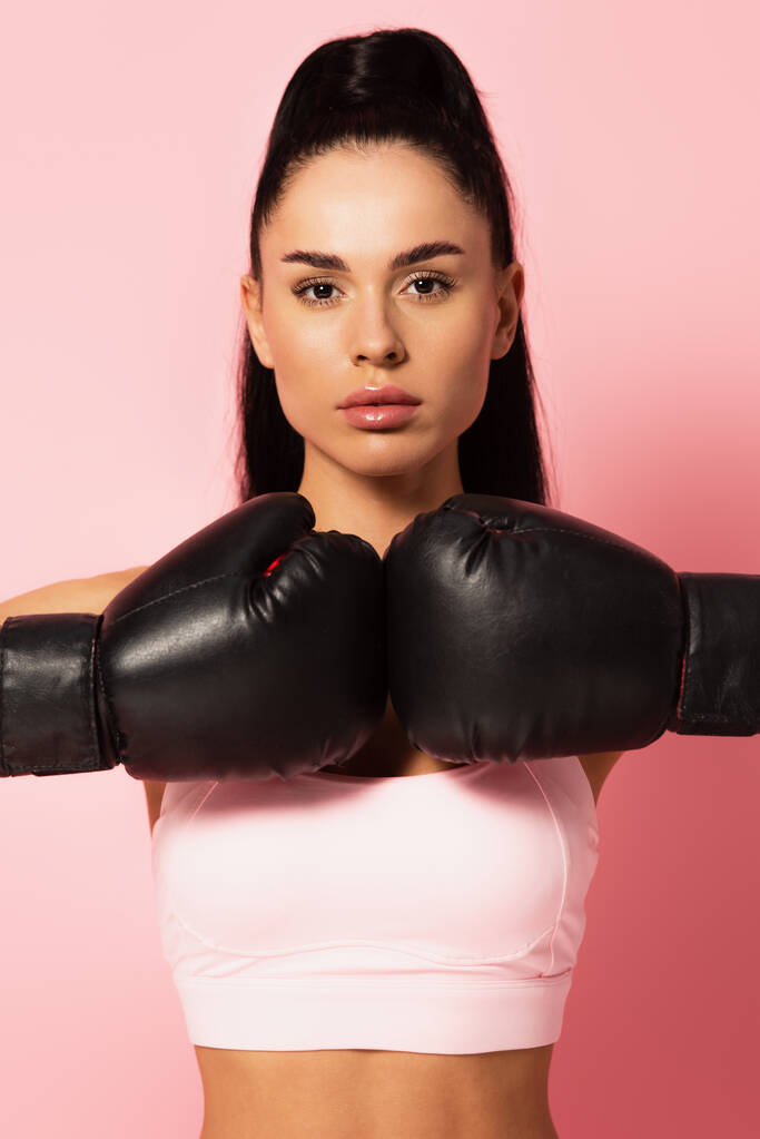 silna kobieta w odzieży sportowej i rękawiczki bokserskie patrząc w aparat fotograficzny na różowy  - Zdjęcie, obraz