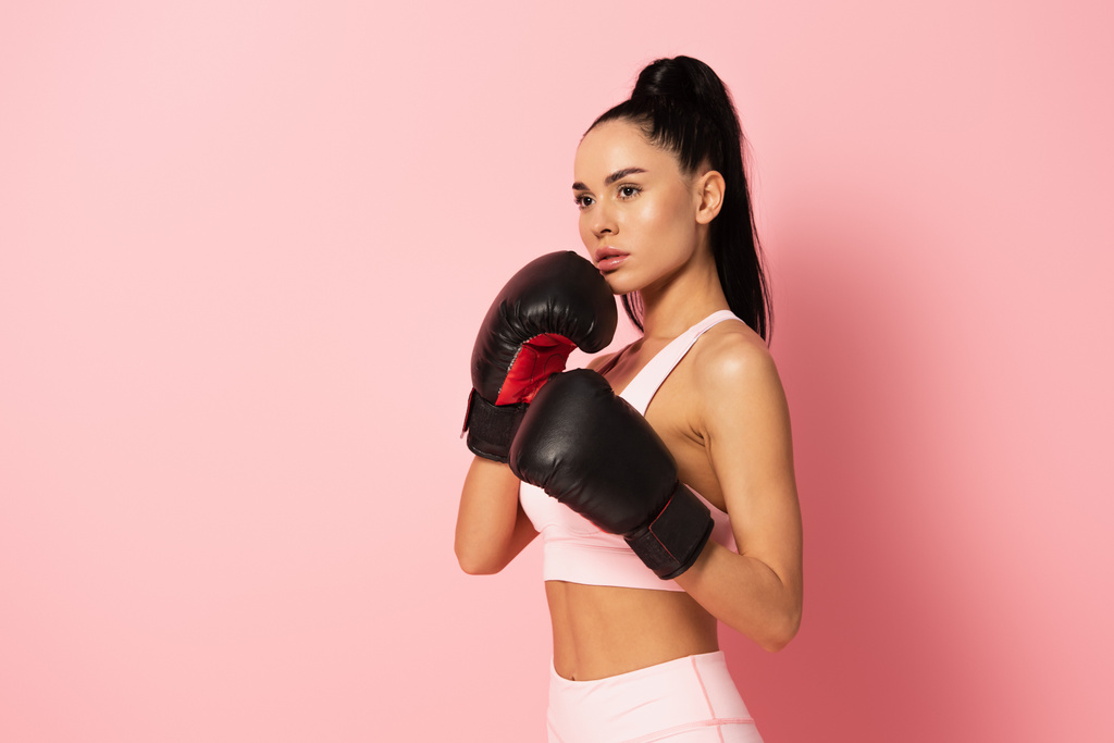 сильная женщина в спортивной одежде и боксерских перчатках на розовом  - Фото, изображение