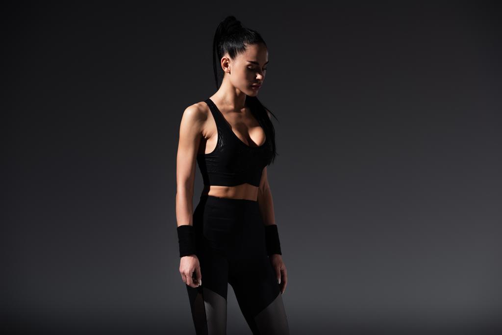 mladá sportovkyně v černé sportovní oblečení stojící na tmavém pozadí  - Fotografie, Obrázek