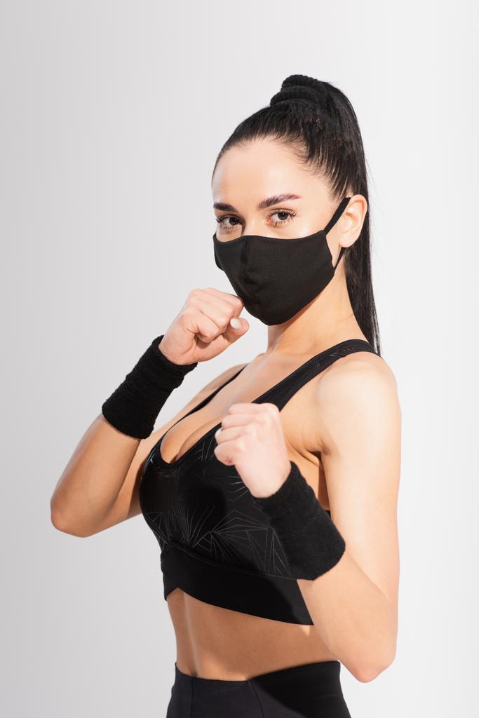 молодой боец в спортивной одежде и черной защитной маске с сжатыми кулаками на сером - Фото, изображение