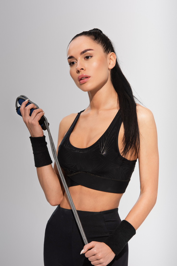 young sportive woman holding skipping rope on grey - Photo, Image