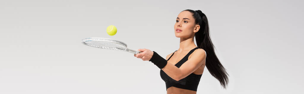 молодая спортсменка, держащая теннисную ракетку и мяч, играя изолированно на сером, баннере - Фото, изображение