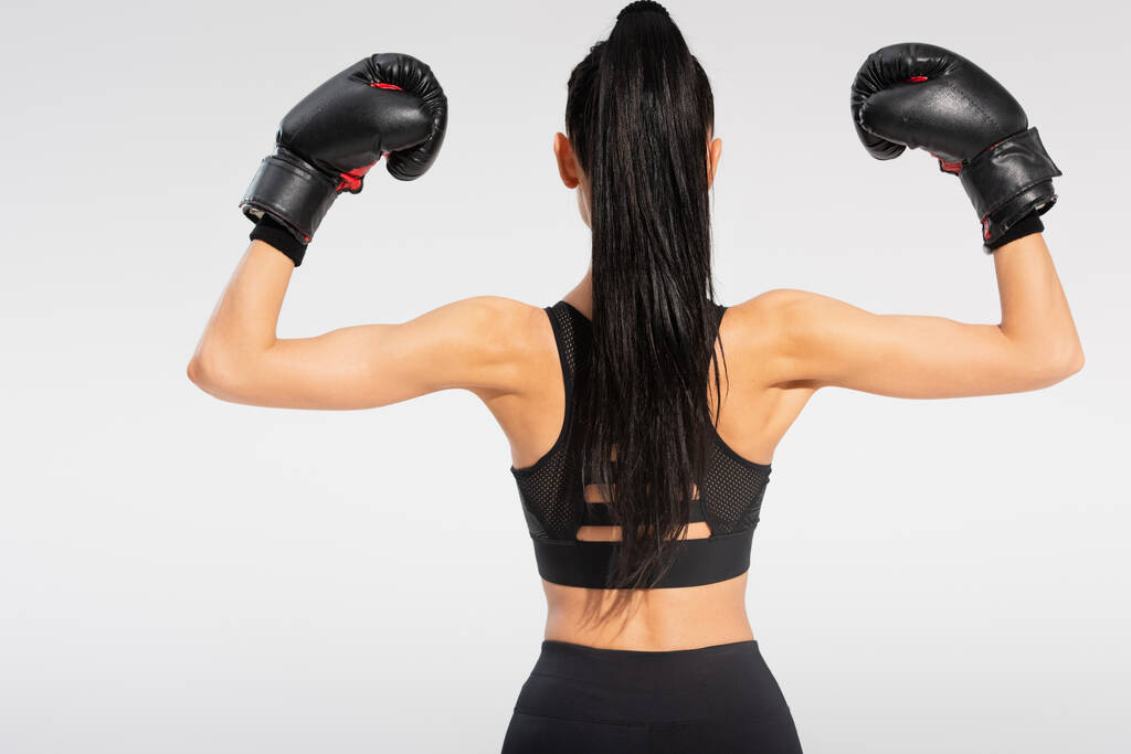 πίσω όψη μελαχρινή νεαρή αθλήτρια σε γάντια πυγμαχίας απομονωμένη σε γκρι - Φωτογραφία, εικόνα