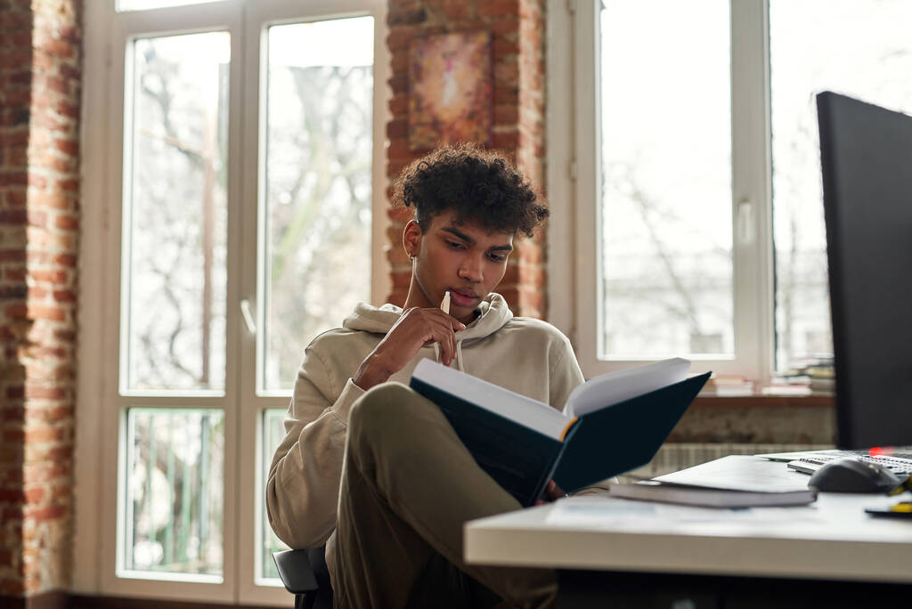 Pensive biracial człowiek czytać książki w domu pracy - Zdjęcie, obraz