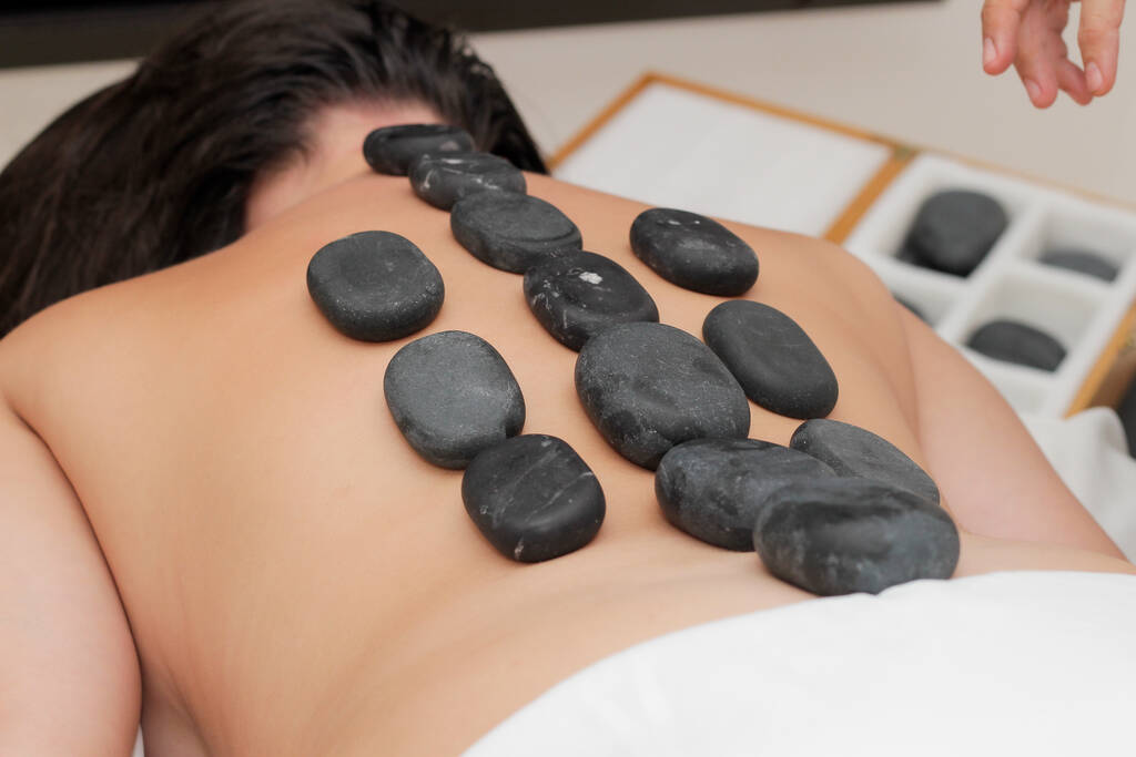 Een close-up shot van een masseur zetten hete stenen voor massage op een vrouw liggend op haar buik - Foto, afbeelding