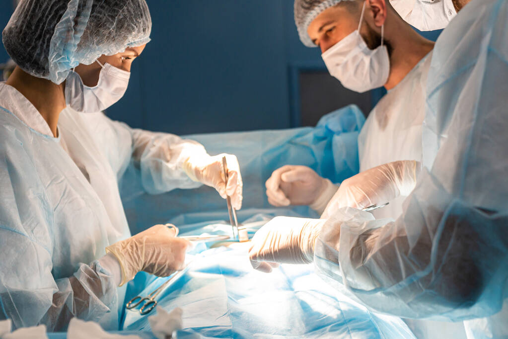 An international team of doctors performs a complex surgical operation on a patient under anesthesia. Modern operating room and experienced surgeons save lives - Photo, Image