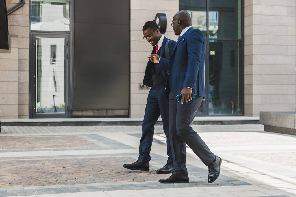 Due uomini d'affari afroamericani dalla pelle scura in giacca e cravatta escono in città e discutono di affari. - Foto, immagini