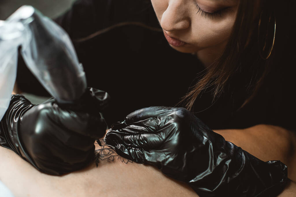 Profesional artista del tatuaje femenino hace un tatuaje en el estudio, de cerca. Fotografía oscura - Foto, imagen