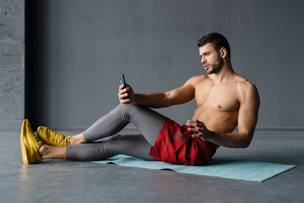 Jovem desportista sem camisa tomando selfie no telefone celular enquanto trabalhava fora dentro de casa - Foto, Imagem