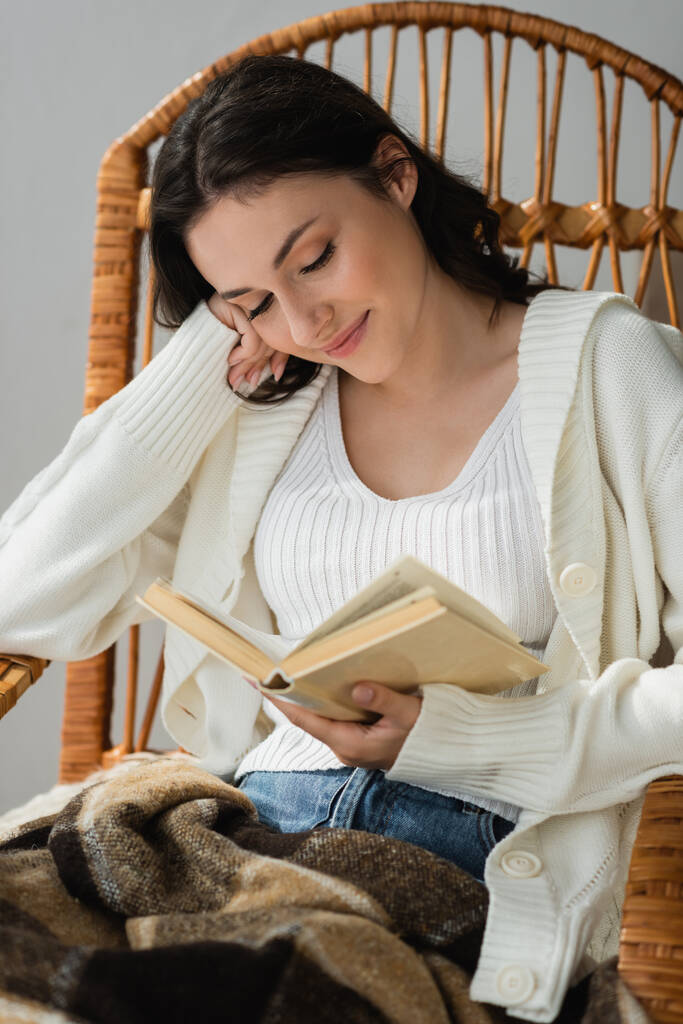 šťastná mladá žena sedí v proutěném křesle a čte román - Fotografie, Obrázek