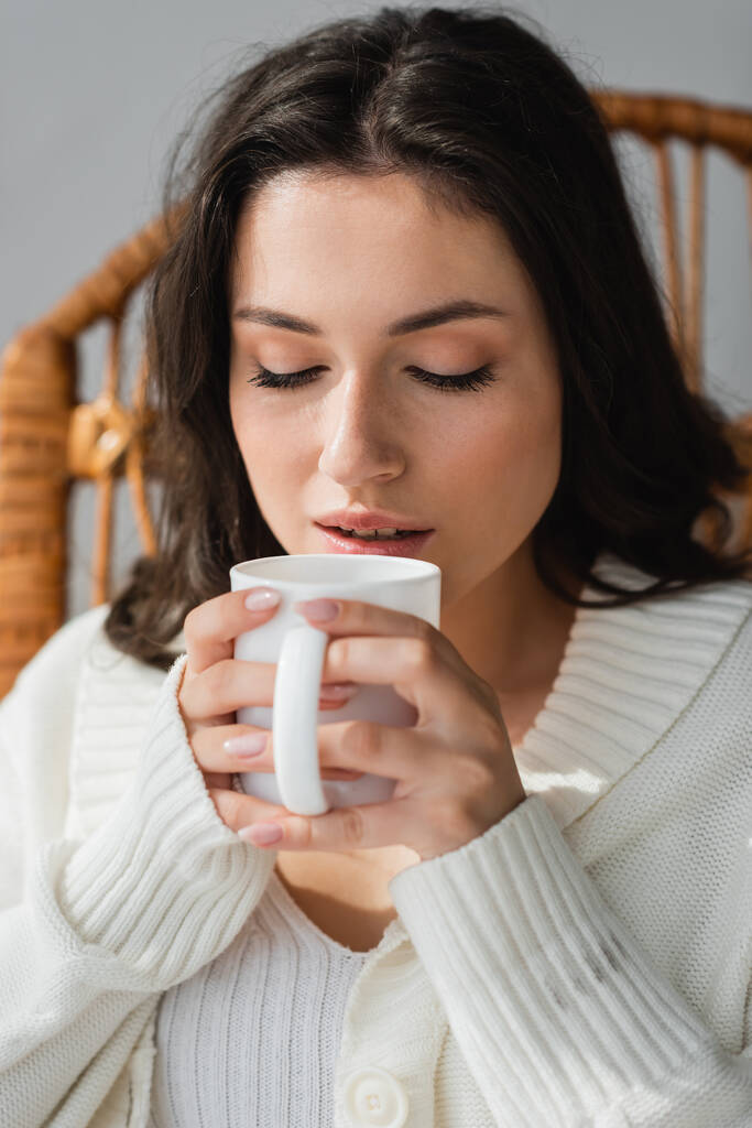 brunette woman in warm cardigan enjoying warm tea with closed eyes - Photo, Image