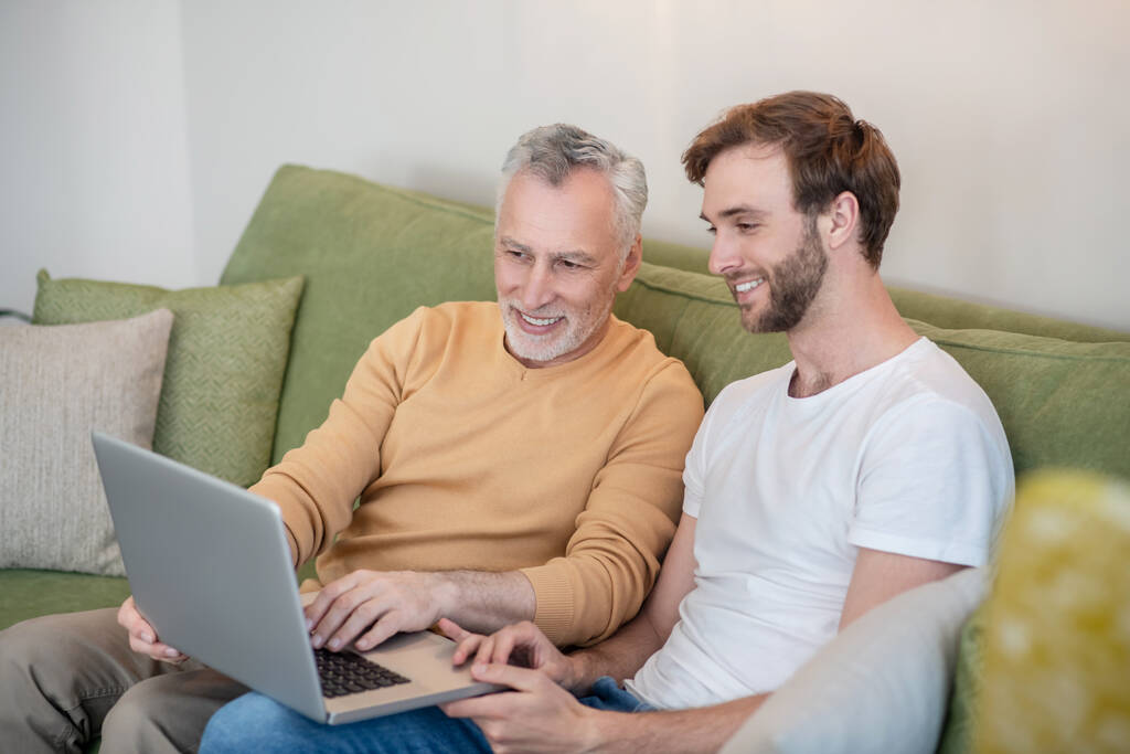Joven hombre y su padre viendo algo en línea y buscando involucrado - Foto, imagen