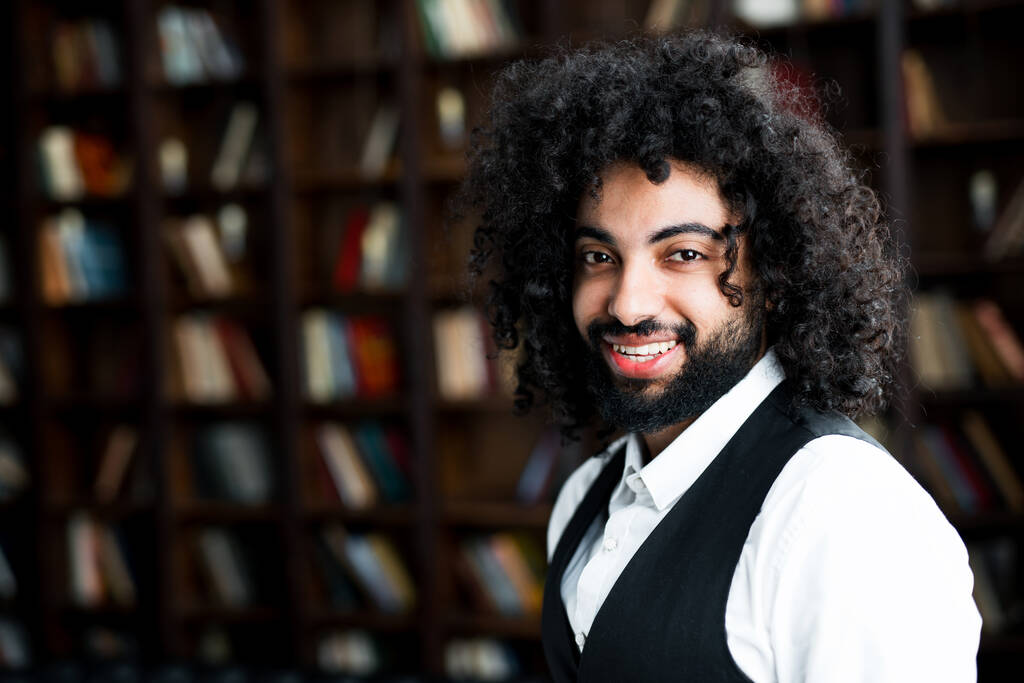 Egy afro-amerikai férfi göndör hajjal, széles mosollyal, aki a könyvtárban áll. - Fotó, kép