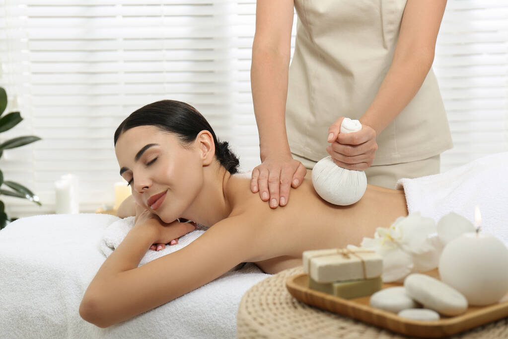 Giovane donna che riceve massaggio borsa a base di erbe nel salone spa - Foto, immagini