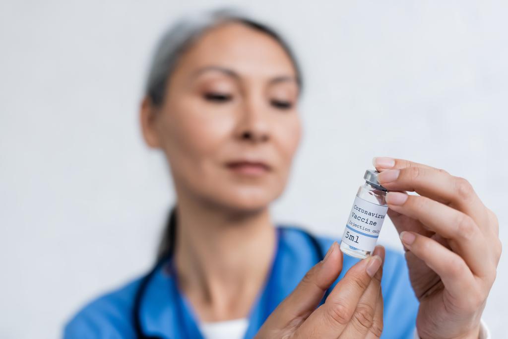 desfocado asiático médico segurando frasco para injetáveis com vacina coronavírus - Foto, Imagem